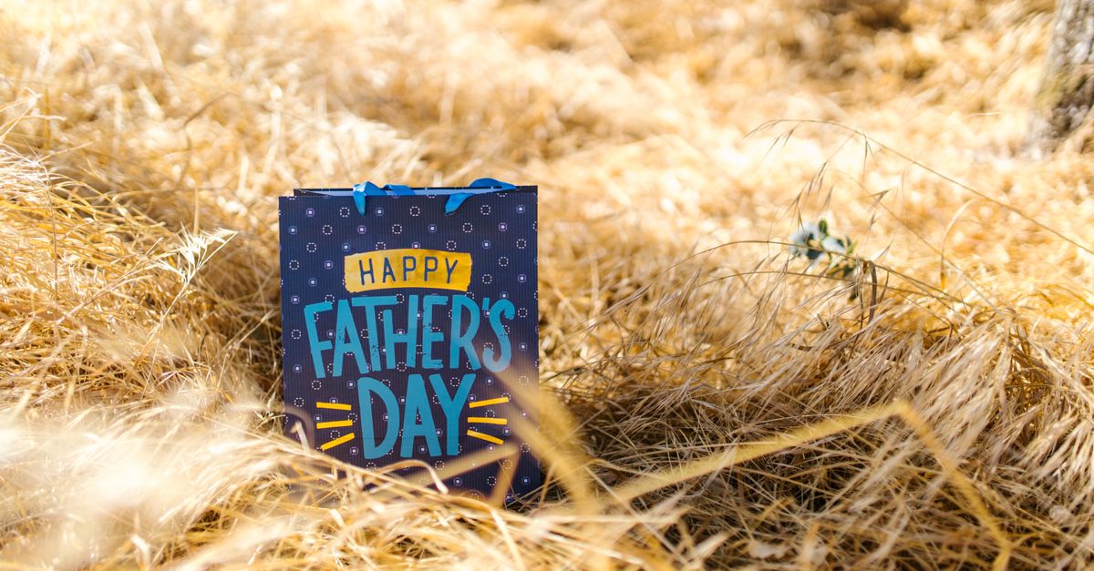 Padre e bambino sorridenti durante la Festa del Papà con un regalo incartato su un tavolo di legno