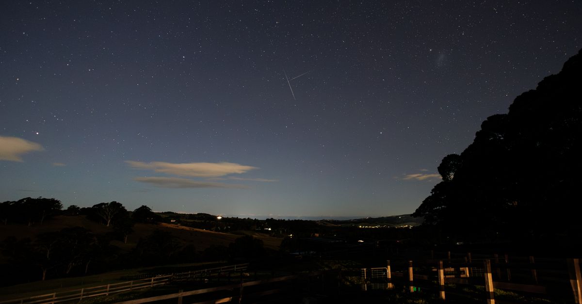 Starry sky crossed by several satellite trails above a dark rural landscape in France
